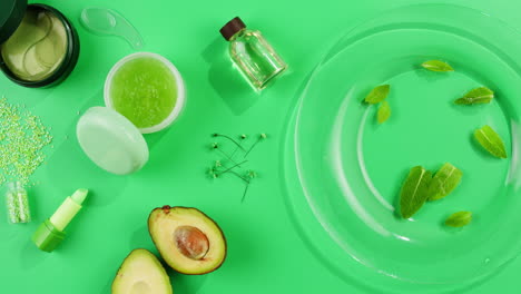 Fresh ripe avocados with cream and essential oil on green background with mint mentol, make up cosmetics