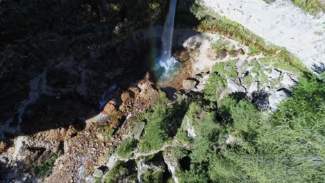 Descending-aerial-view-of-an-isolated-waterfall-forming-a-small-stream-in-the-middle-of-thick-dense-forest