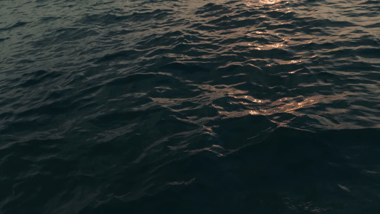 Slow motion shot of golden sun reflecting during sunset in water waves of blue ocean