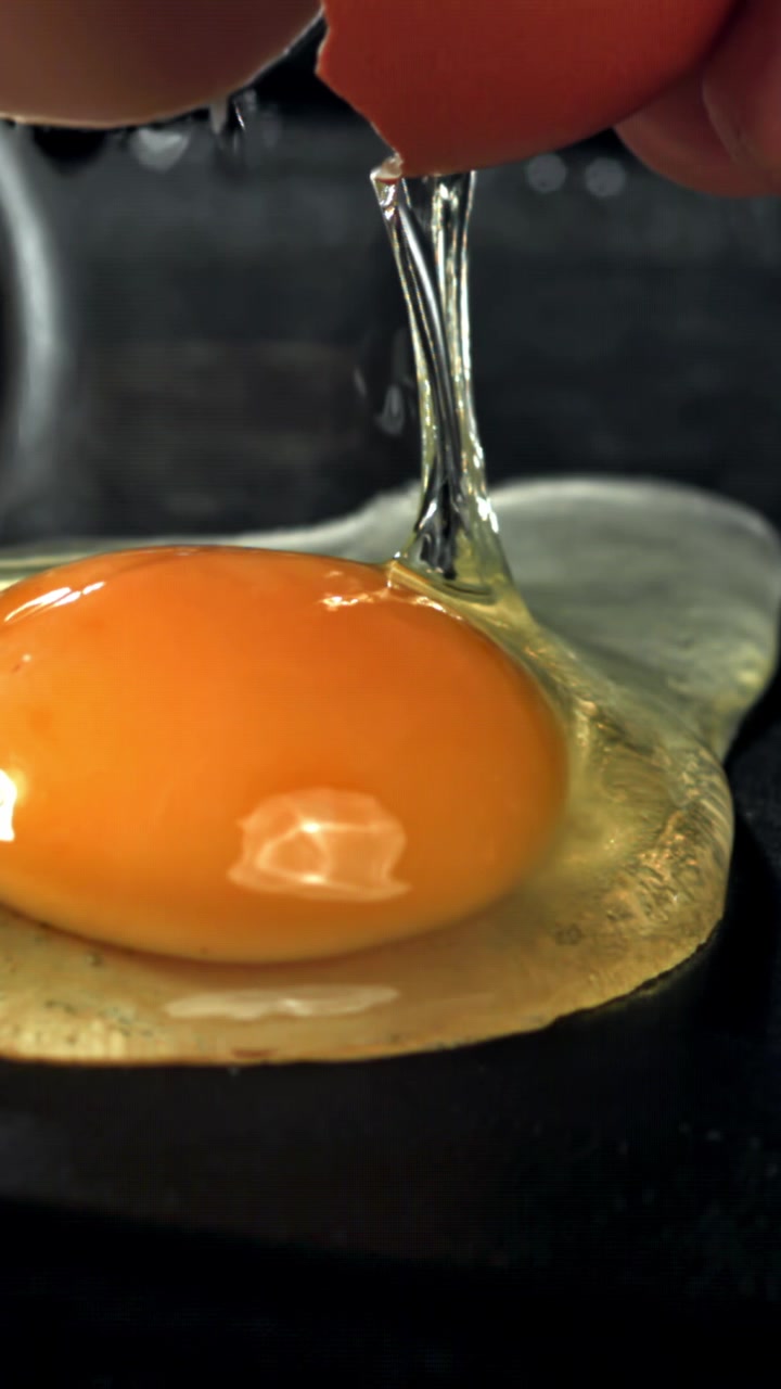 Close-up of a Raw Egg Cracking and Separating on a Dark Surface