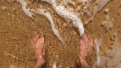 close up shot of sea water moving around the feet of a man on a sand beach