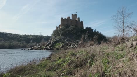 spectacular scenic view of medieval castle of almourol atop islet in middle of tagus river water, praia do ribatejo, on sunny blue sky day, portugal, handheld pan up