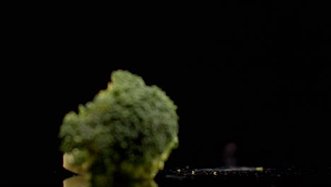 one fresh green broccoli falling on a glass with splashes and drops of water in slow motion