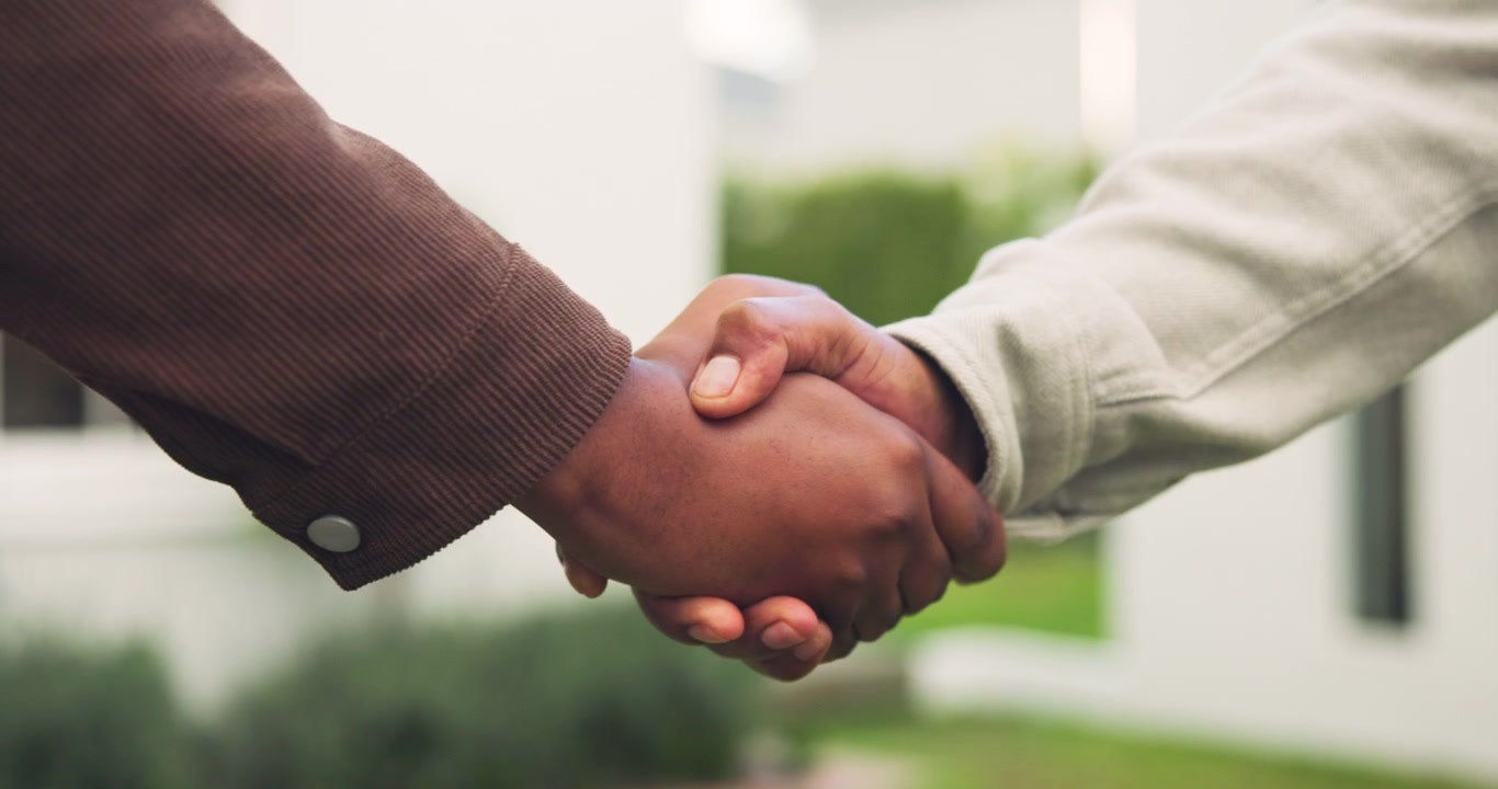 Two People Shaking Hands Outdoors in Front of a Modern House