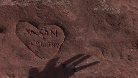 Der-Schatten-Einer-Hand-Bewegt-Sich-über-Ein-In-Sandstein-Gehauenes-Graffiti-Herz