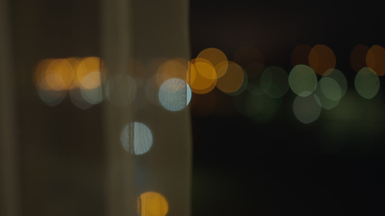 Blurry lights of the night city from an open window, behind the curtains