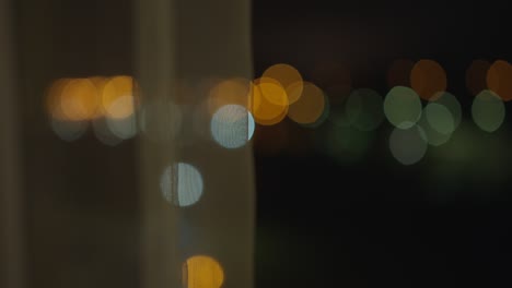 blurry lights of the night city from an open window, behind the curtains