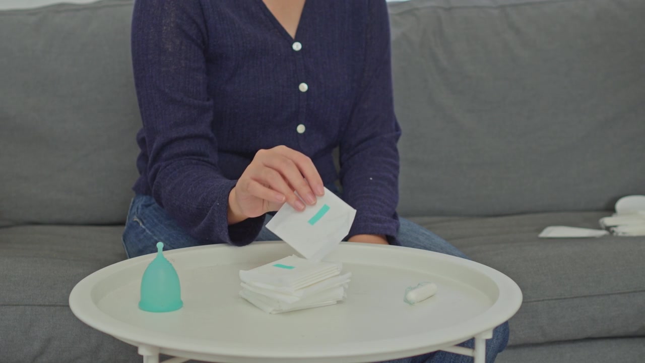 Primo piano di una donna che tocca prodotti per l'igiene femminile prima di scegliere un assorbente.