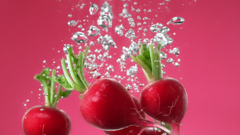 radishes dropped into water make bubbles and sink to bottom on rose background, macro and slow motion