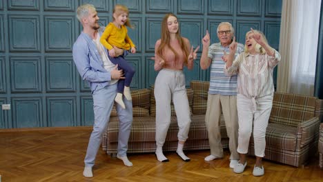 family members of different generations having fun listening music, dancing crazy in room at home