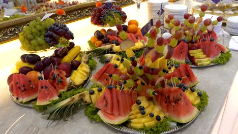 a table with fruits, platters of pineapple, watermelon, bananas, melon, and grapes