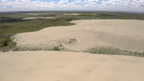 dry arid desert sand dunes in expansive flat plains landscape on sunny blue sky day, sandhills, saskatchewan, canada, overhead aerial pull back