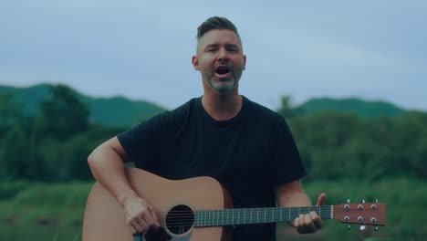 man singing and playing acoustic guitar outdoors