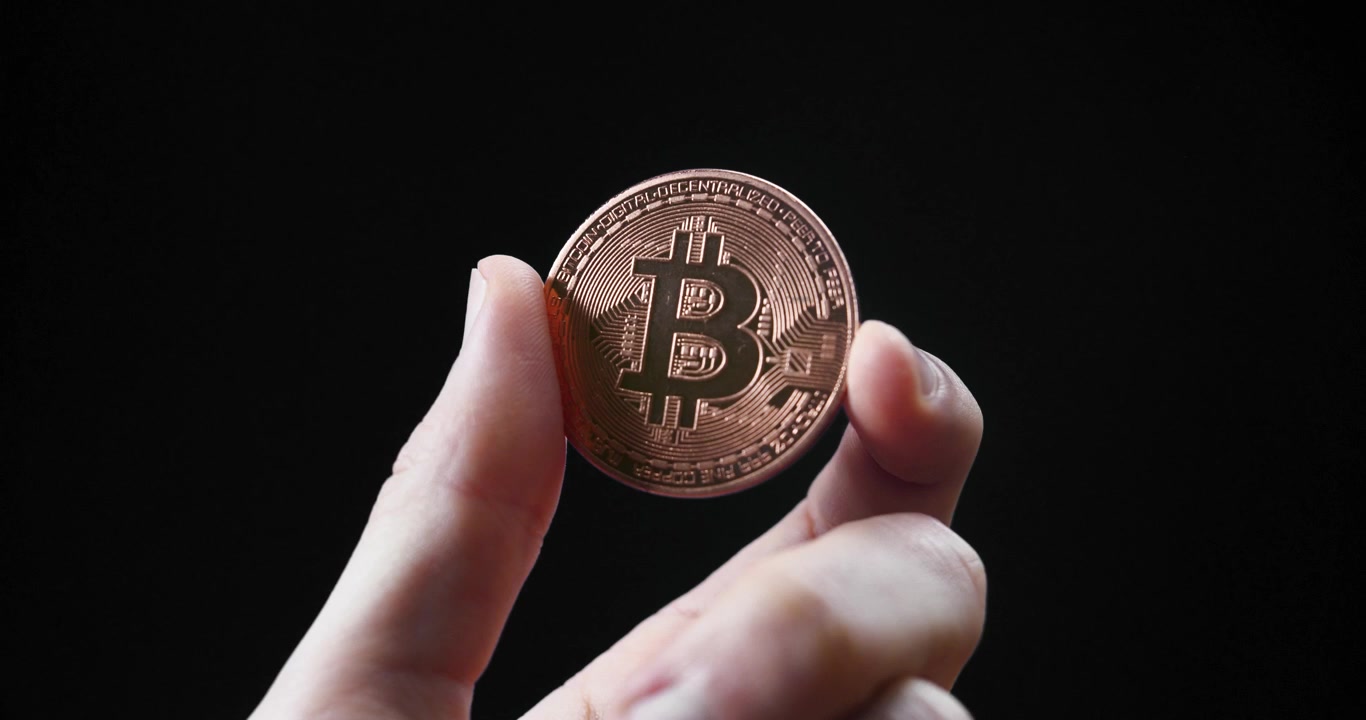 Mano che tiene una moneta Bitcoin su sfondo nero, a simboleggiare la valuta digitale.