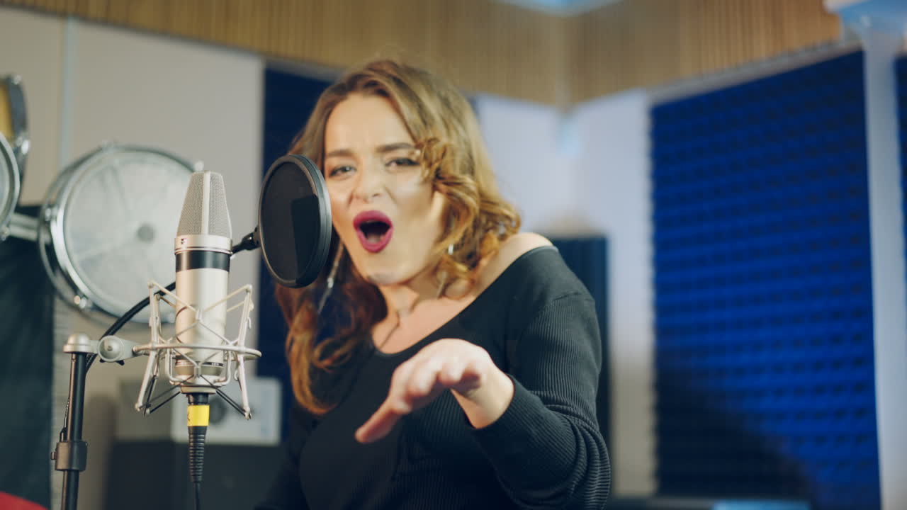 Young female singer recording album in the professional studio. Woman singing a song in music recording studio.