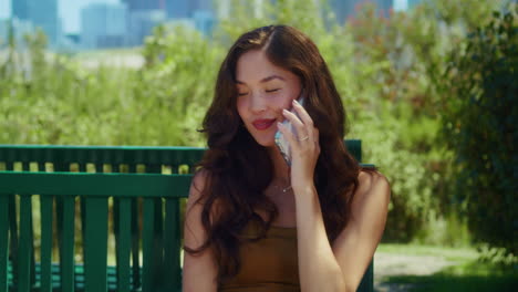 smiling girl speaking phone on park bench closeup. asian woman holding gadget.