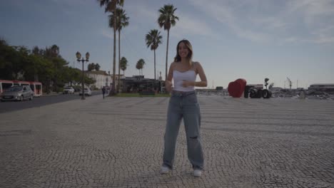 Caucasian-woman-dancing-on-an-ancient-square-in-Faro,-Portugal,-with-palm-trees