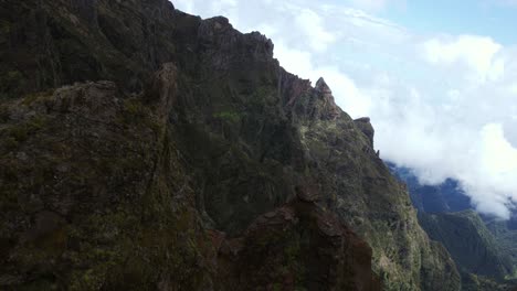 dramatic aerial shot of rugged mountain cliffs at pico do arieiro in madeira, portugal, with clouds rolling over the peaks and deep shadows enhancing the dramatic landscape
