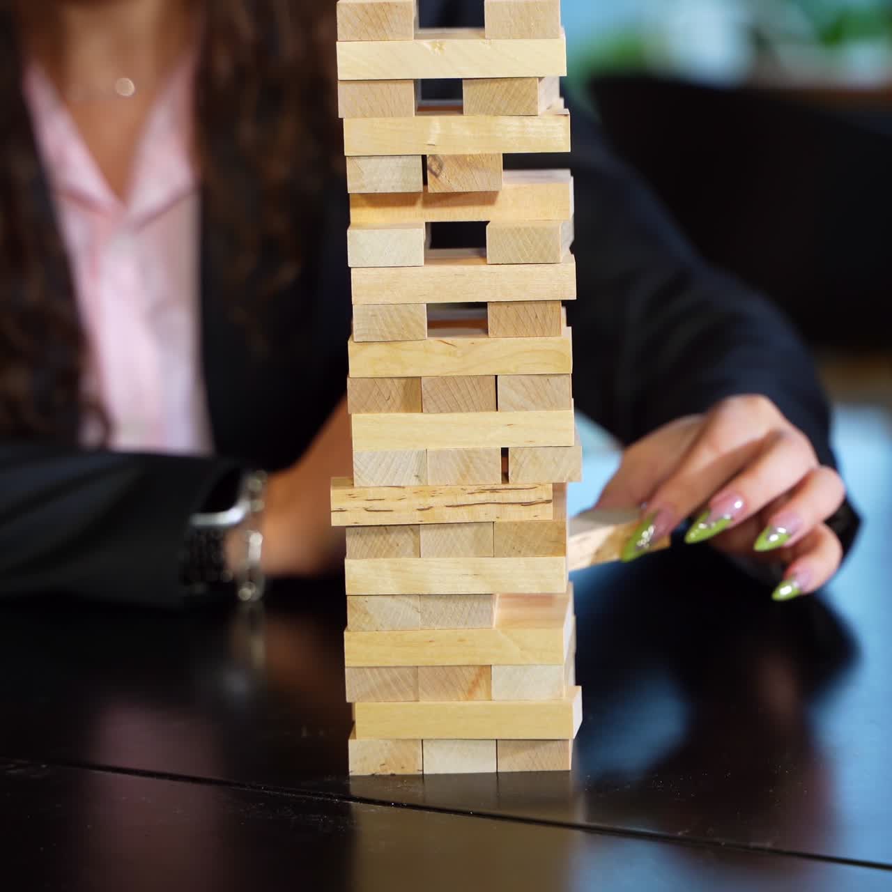 Little wooden bricks stacked up in a pile. People play jenga at the black table. Blurred background