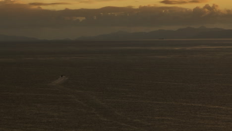barco de pesca navegando a través de la bahía de tasmania durante las primeras horas de la mañana con el amanecer a punto de aparecer sobre las montañas, nueva zelanda