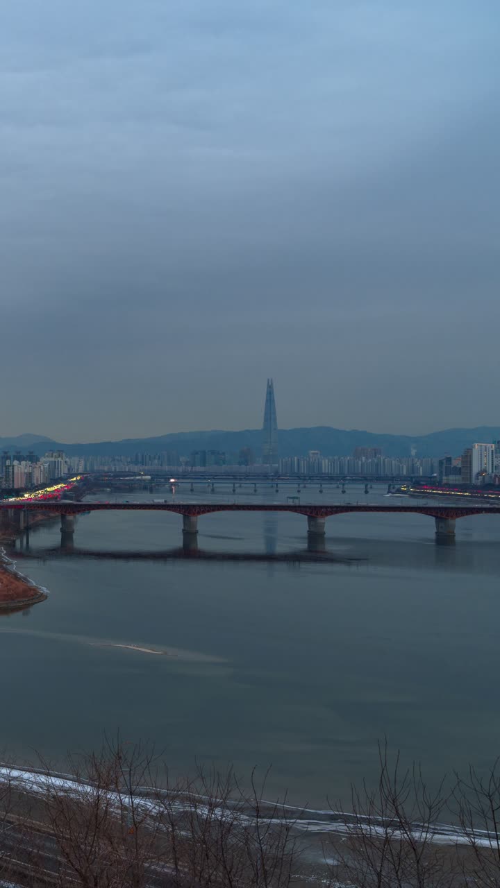 Time-lapse aereo diurno del ponte Seongsu che attraversa il fiume Han a Seoul, con il grattacielo Lotte World Tower e lo sfondo nebbioso dello skyline della città, verticale