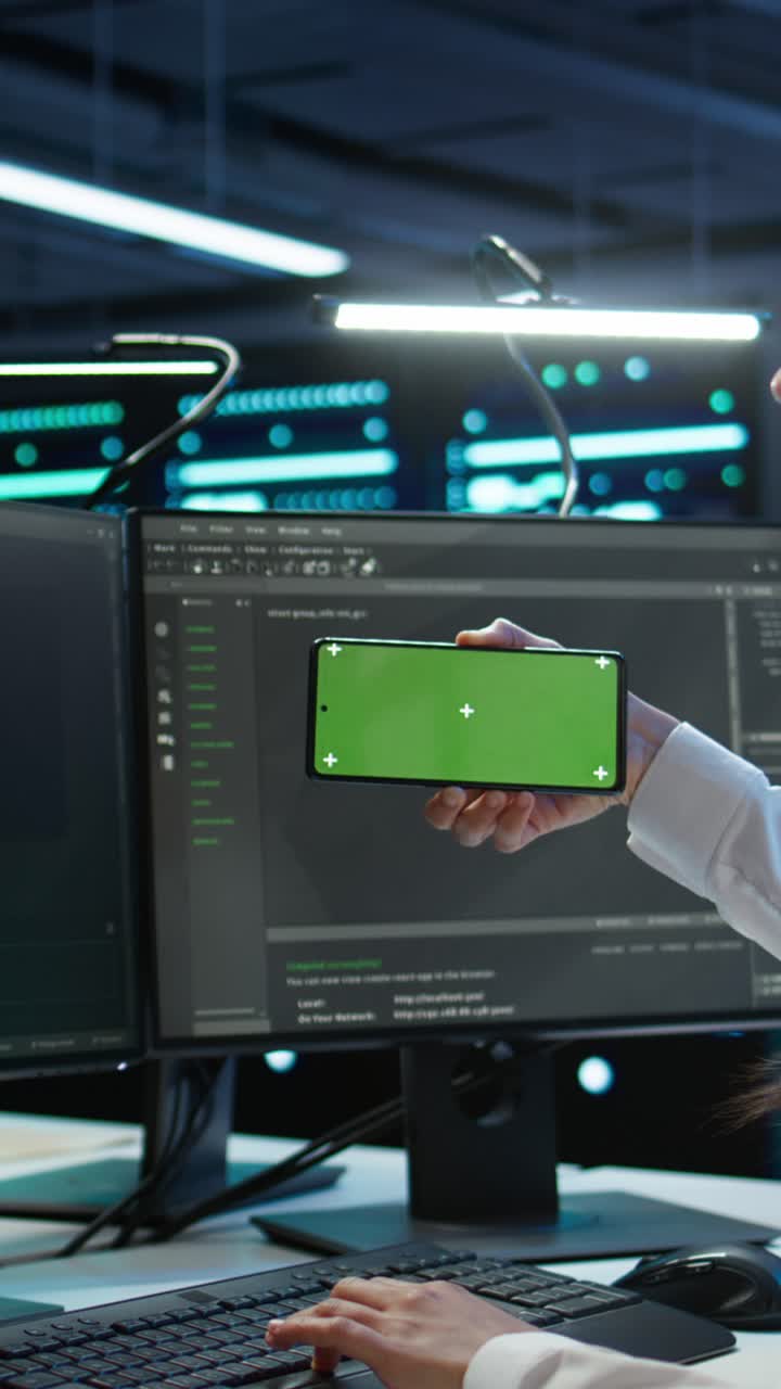 Developer Holding Green Screen Smartphone While Typing on Computer
