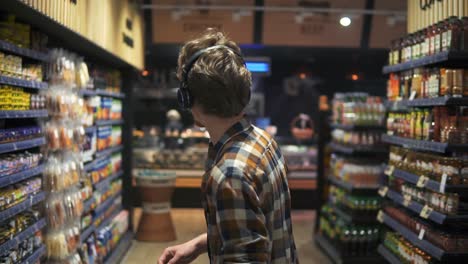 at the supermarket: stylish caucasian guy with headphones walks through goods section of the store, wearing plaid shirt