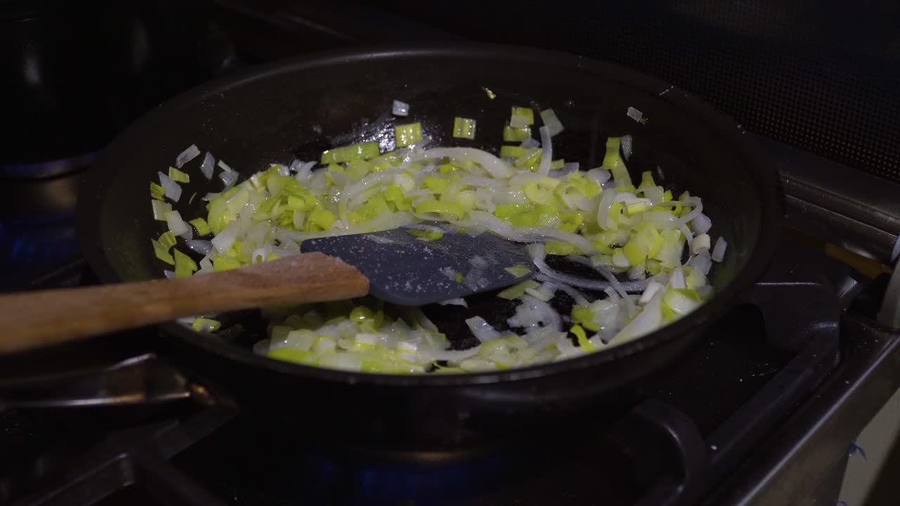 Seasoning leek and onion in frying pan with resting spatula, indoor cooking
