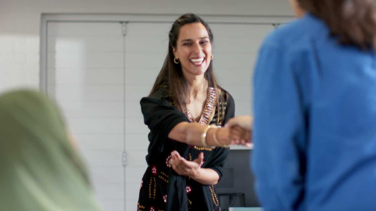 Indian woman thanking colleagues at conference table, rising, shaking colleague in headscarf's hand