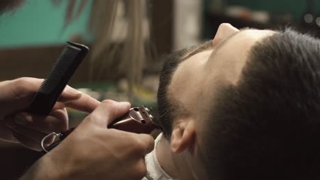 barber trimming a client's beard with an electric trimmer and comb