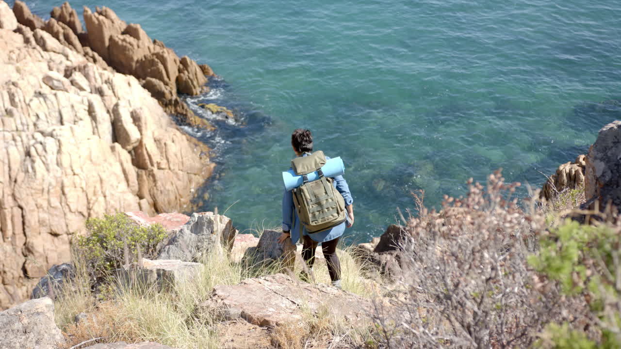 Hiking on mountain trail, person with backpack and yoga mat overlooking ocean