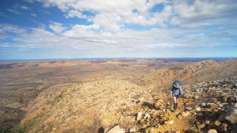 Pan-past-hiker-across-rocky-desert-landscape,-Central-Australia