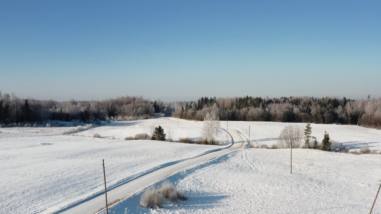 Winter beauty in early morning from above with hoar frost and snow blanket over the landscape. Aerial drone view over a winding gravel road in countryside and frozen forest in the background.