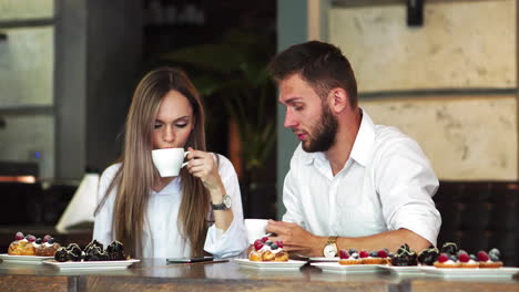 Young-man-pointing-on-girl's-telephone-while-making-booking-online-and-discussing-,male-and-female-colleagues-communicating-on-coffee-break-checking-updated-on-education-web-page-via-smartphone