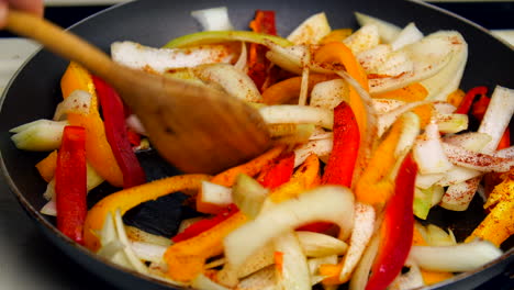 bell peppers and onions get stirred in a frying pan