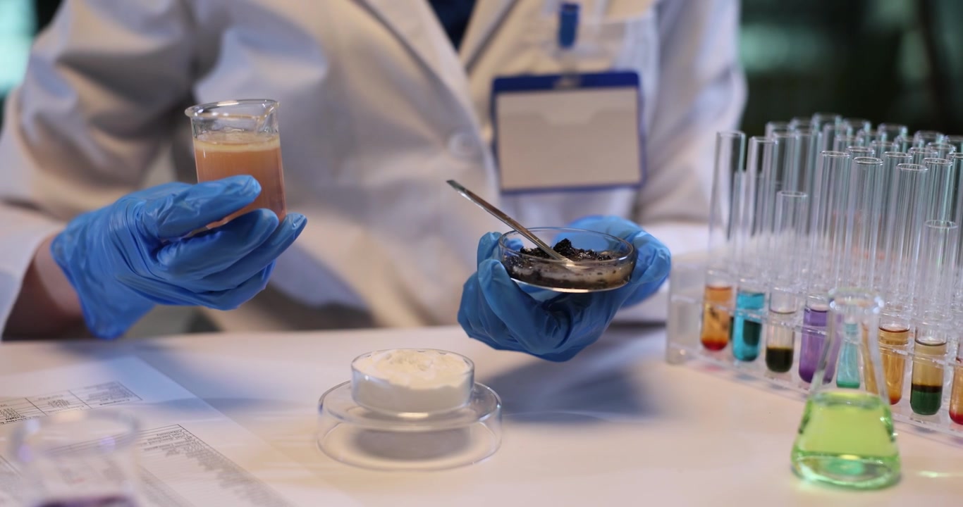 Woman assistant pours liquid on soil sample in petri dish