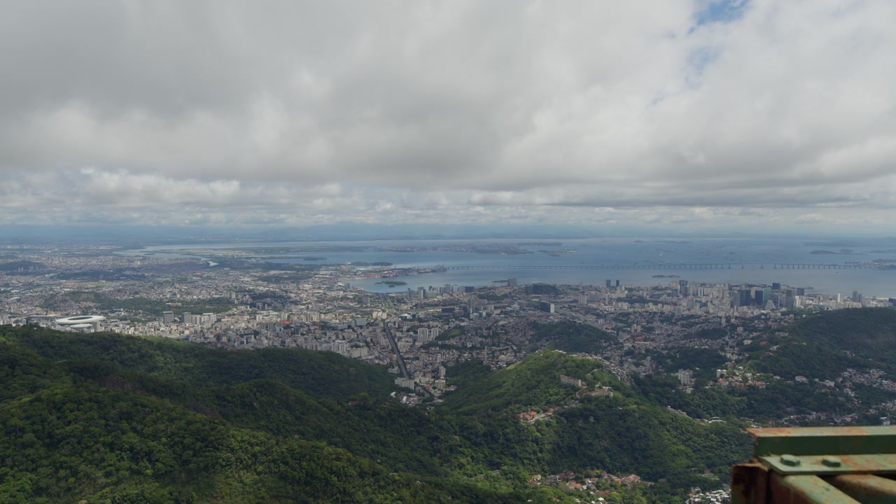 Fitta foresta verde si estende verso la vasta città di Rio de Janeiro, che si protende fino a un orizzonte sfocato sotto una fitta nuvolosità