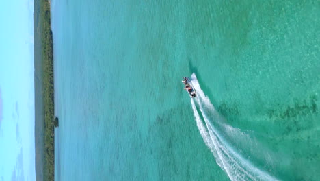 seguimiento aéreo de una lancha a motor por la isla de los pinos, aguas cristalinas de nueva caledonia - video vertical