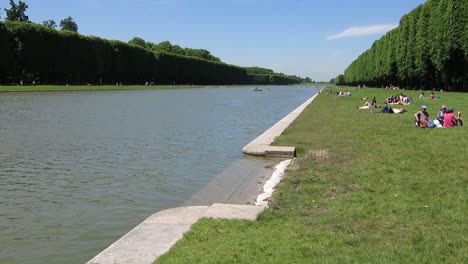 Gente-Descansando-A-Orillas-De-Un-Lago,-En-Los-Jardines-Del-Palacio-De-Versalles,-París,-Francia