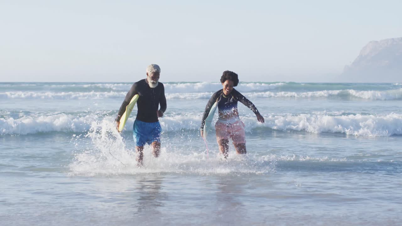 feliz pareja afroamericana corriendo con tablas de surf en una playa soleada