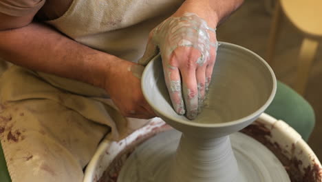 looking down over potter moulding handmade wet ceramic vessel turning on workshop pottery wheel