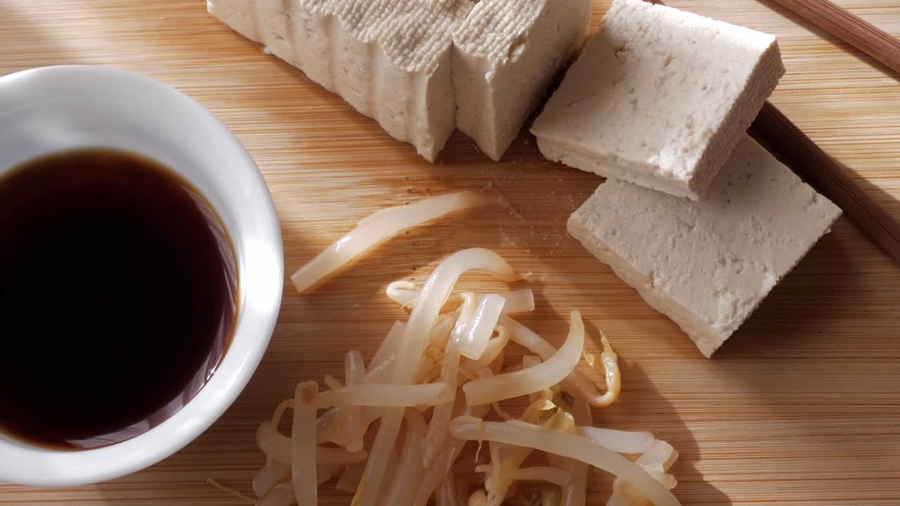 Fresh tofu slices on bamboo board with soy sauce and bean sprouts