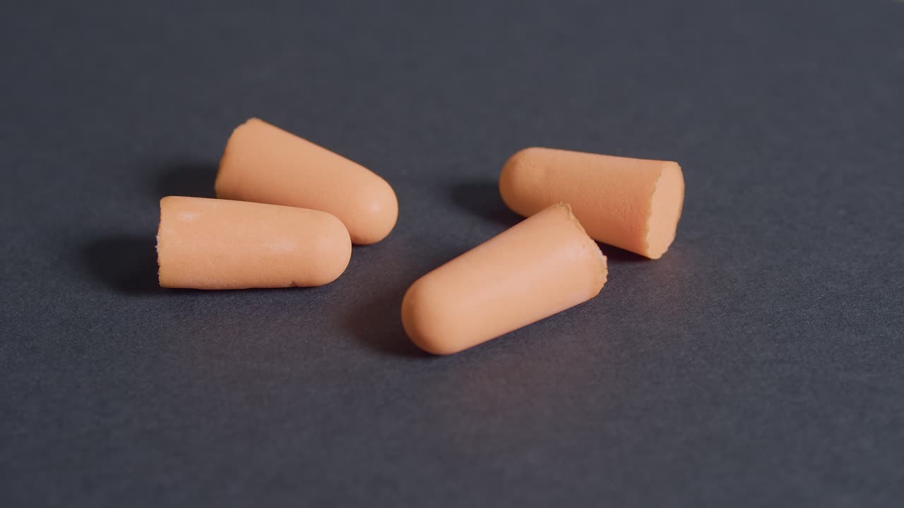 Orange ear plugs, hear protection on dark gray background, rotation view
