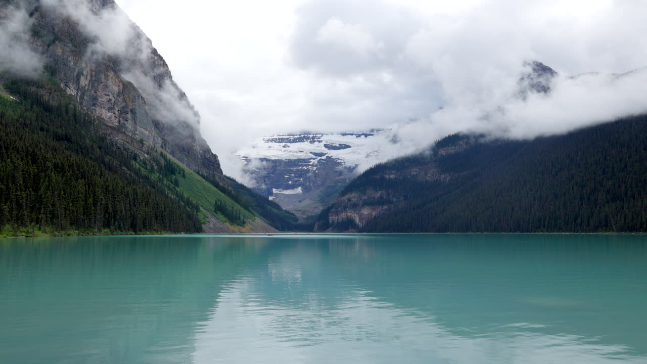 Serene Lake Louise, Canada in overcast weather, surrounded by dramatic peaks and calm turquoise waters