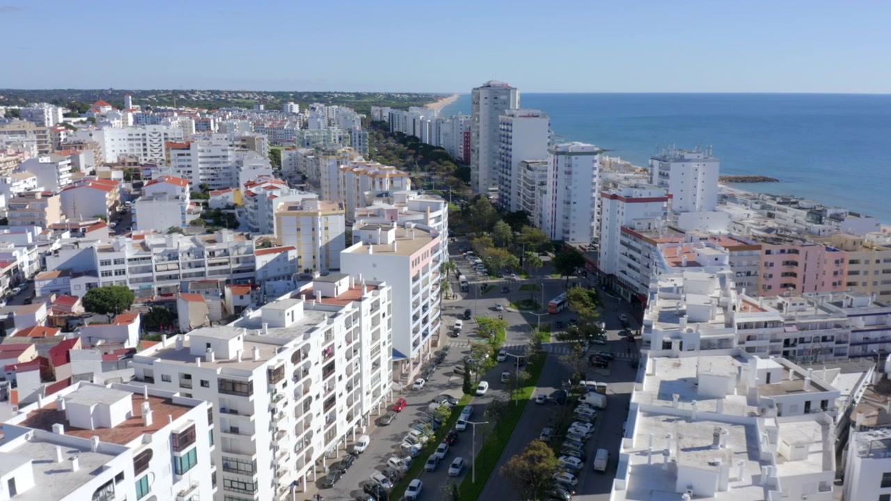 Drone a voar para trás sobre uma avenida arborizada na cidade turística de Quarteira, Algarve.