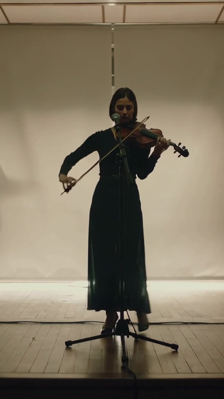 Vertical video: Entering from right violinist in black dress at mic stand bowing violin to perform