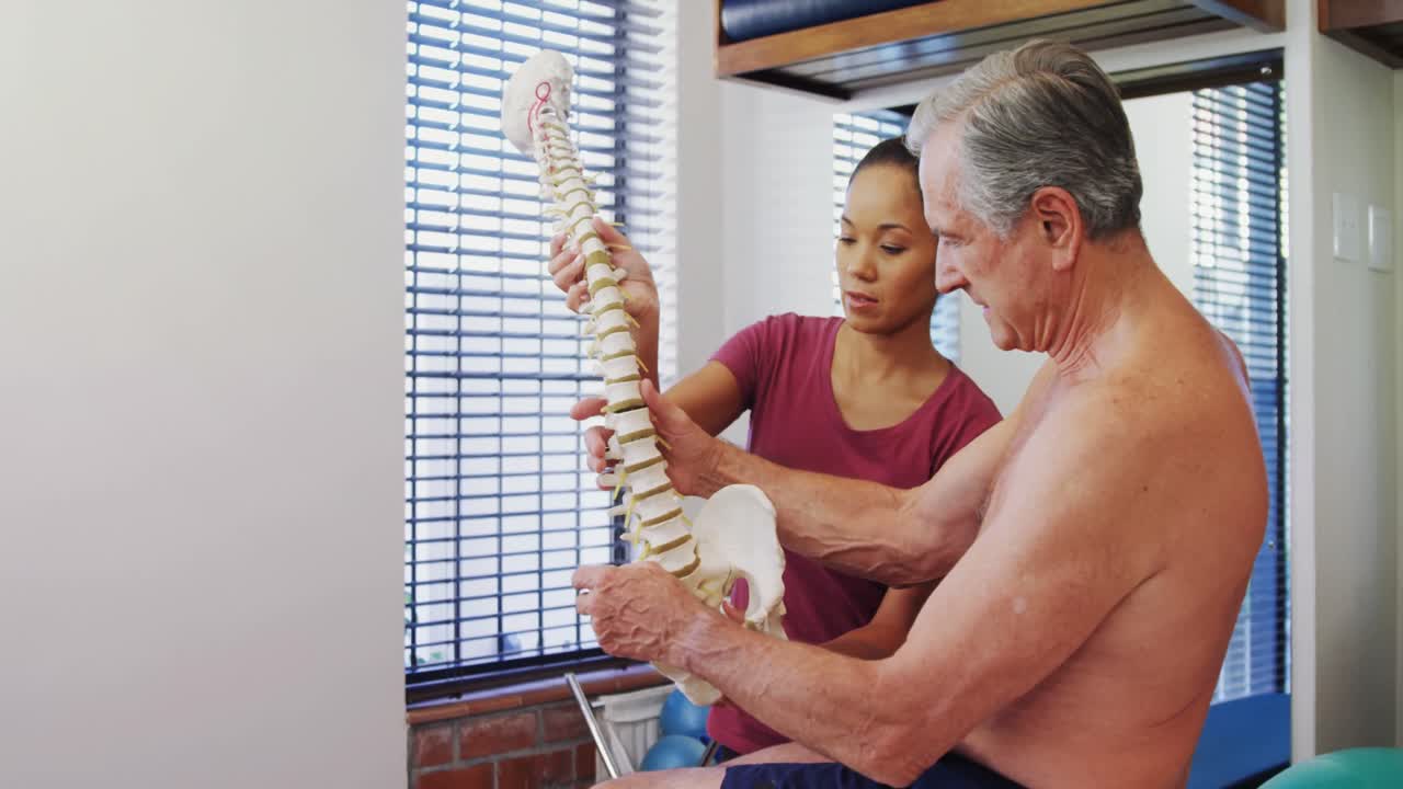 Physiotherapist explaining the spine model to senior patient 4k