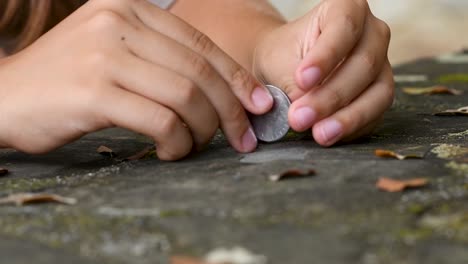 manos de niña girando una moneda en el campo