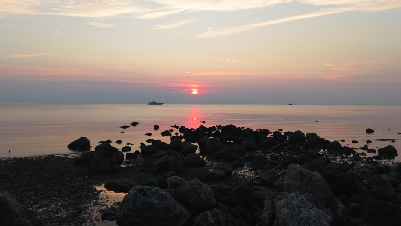 Sunset over the sea with rocks and boats