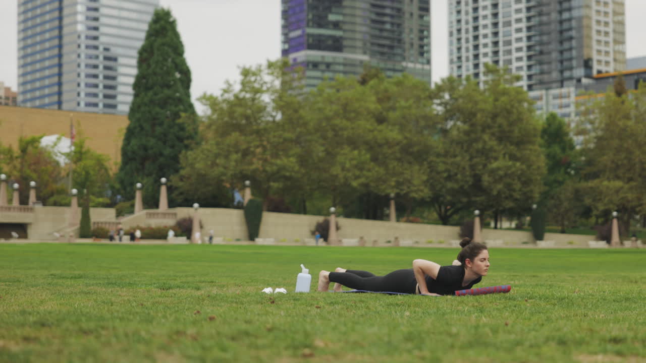 hermosa mujer joven caucásica realizando yoga chaturanga dandasana - perro de tablón hacia arriba - sobre hierba verde en un parque de seattle